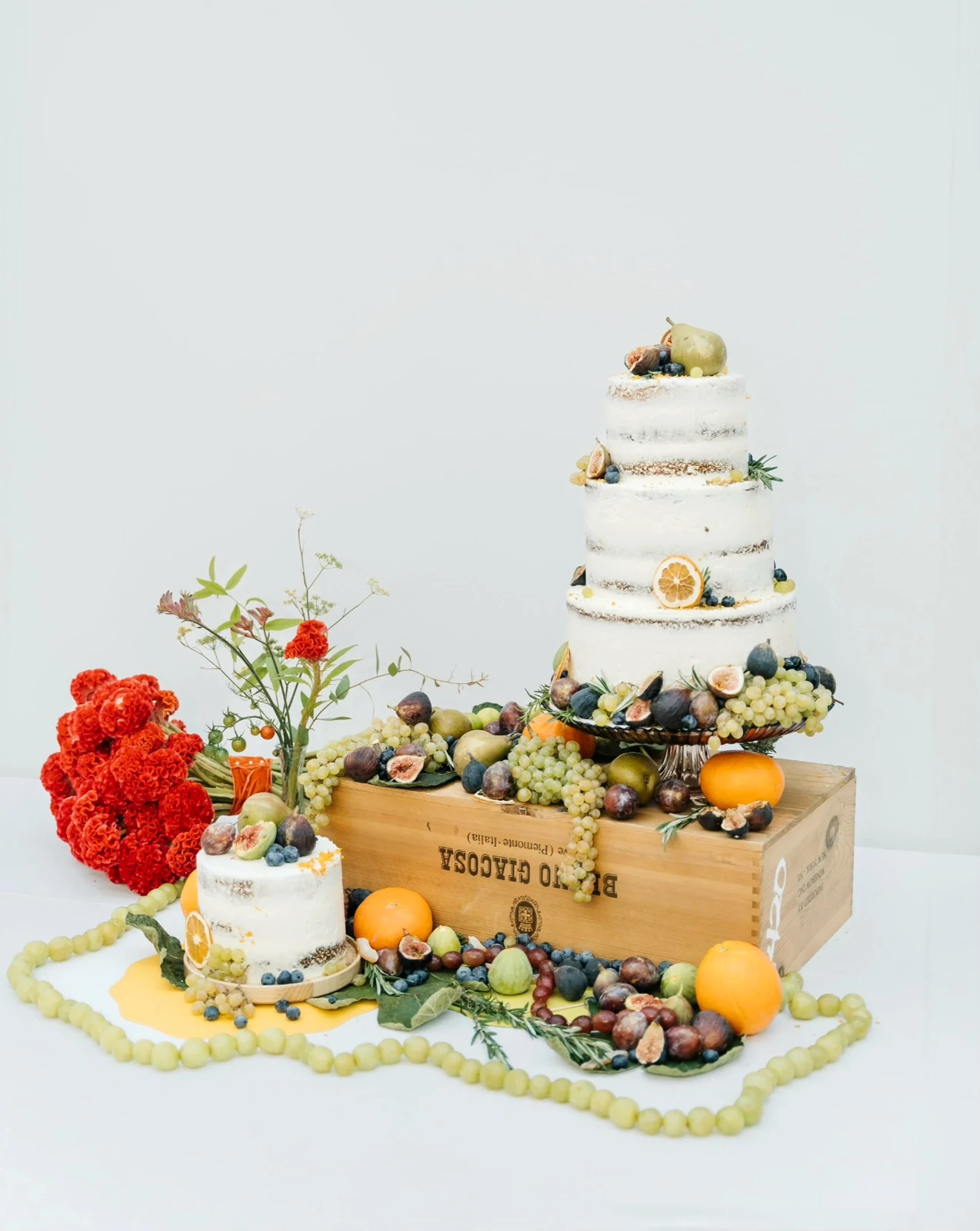 Three-tier semi-naked wedding cake with figs, grapes, citrus and seasonal flowers
